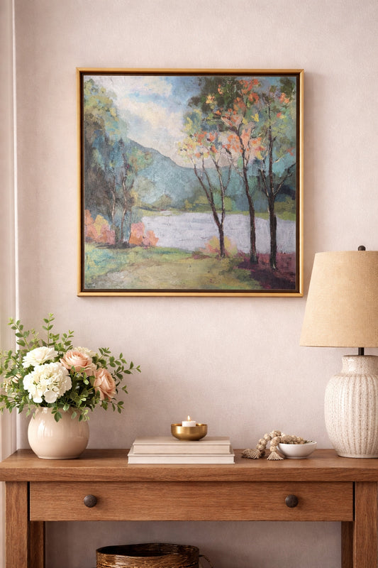Original landscape painting in gold frame styled above a wooden entryway console table with flowers, candle, and lamp
