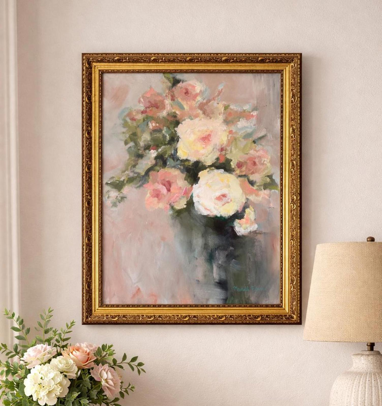 Framed painting of flowers on a wall with a lamp and flowers in the foreground.