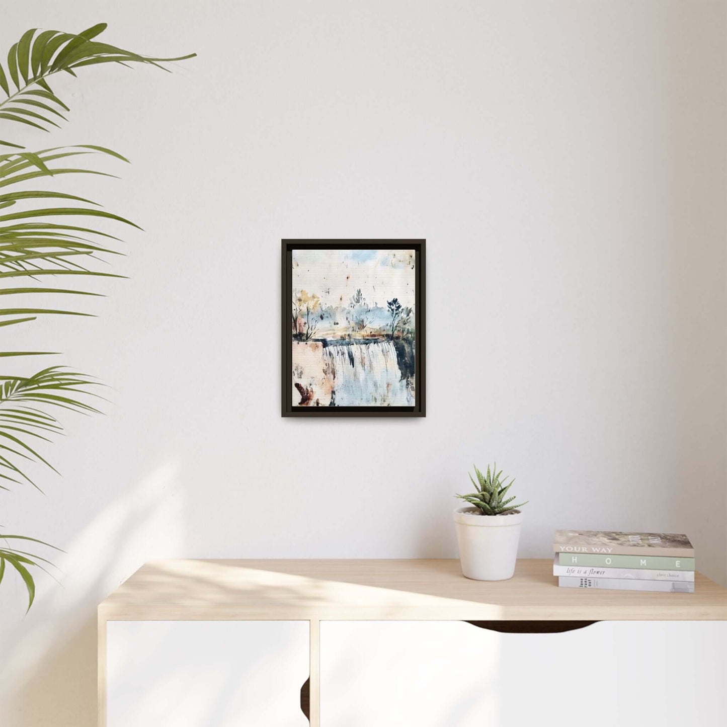 Framed watercolor wall art of serene landscape, displayed in a modern room on a light-colored wall with a potted plant and decorative books.