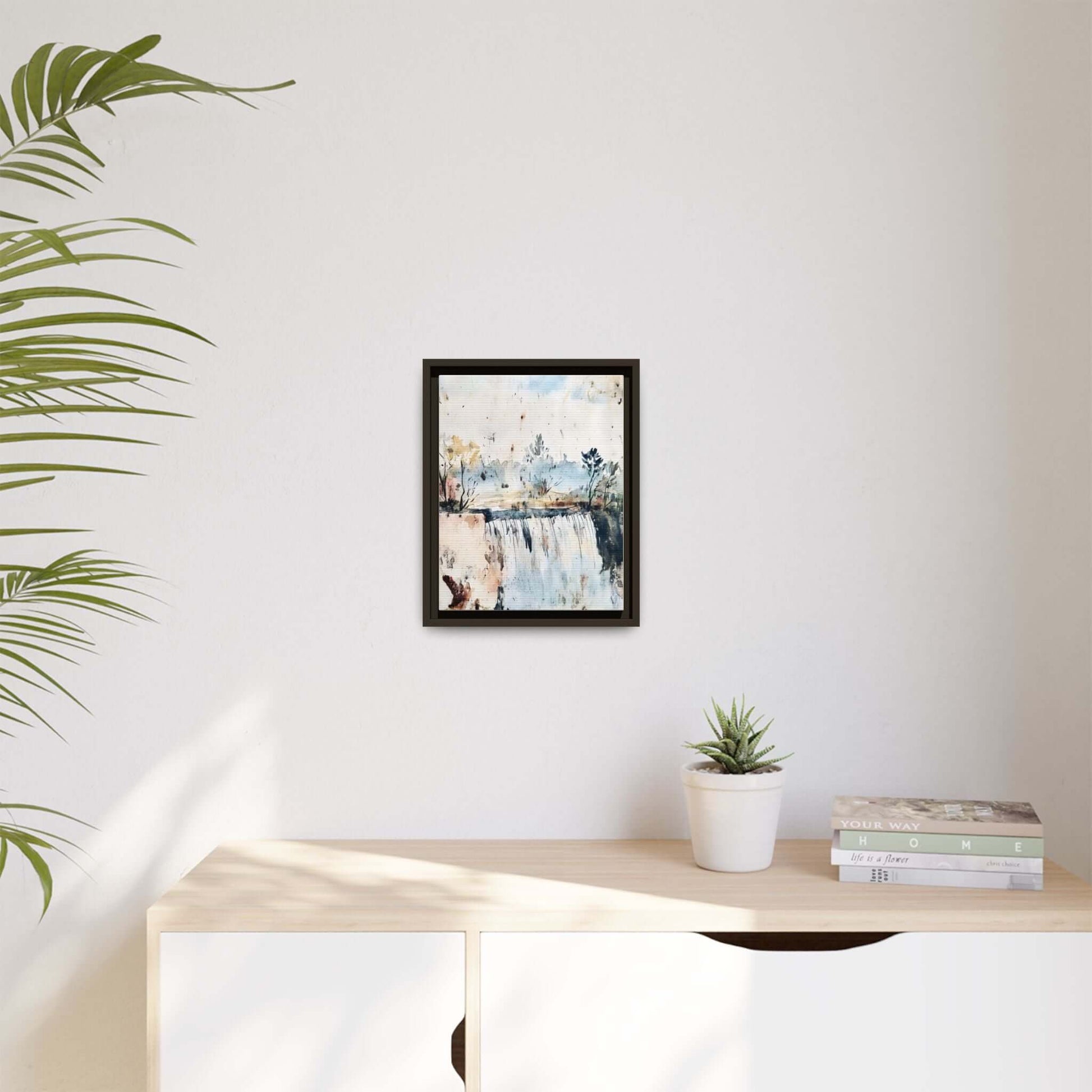 Framed watercolor wall art of serene landscape, displayed in a modern room on a light-colored wall with a potted plant and decorative books.