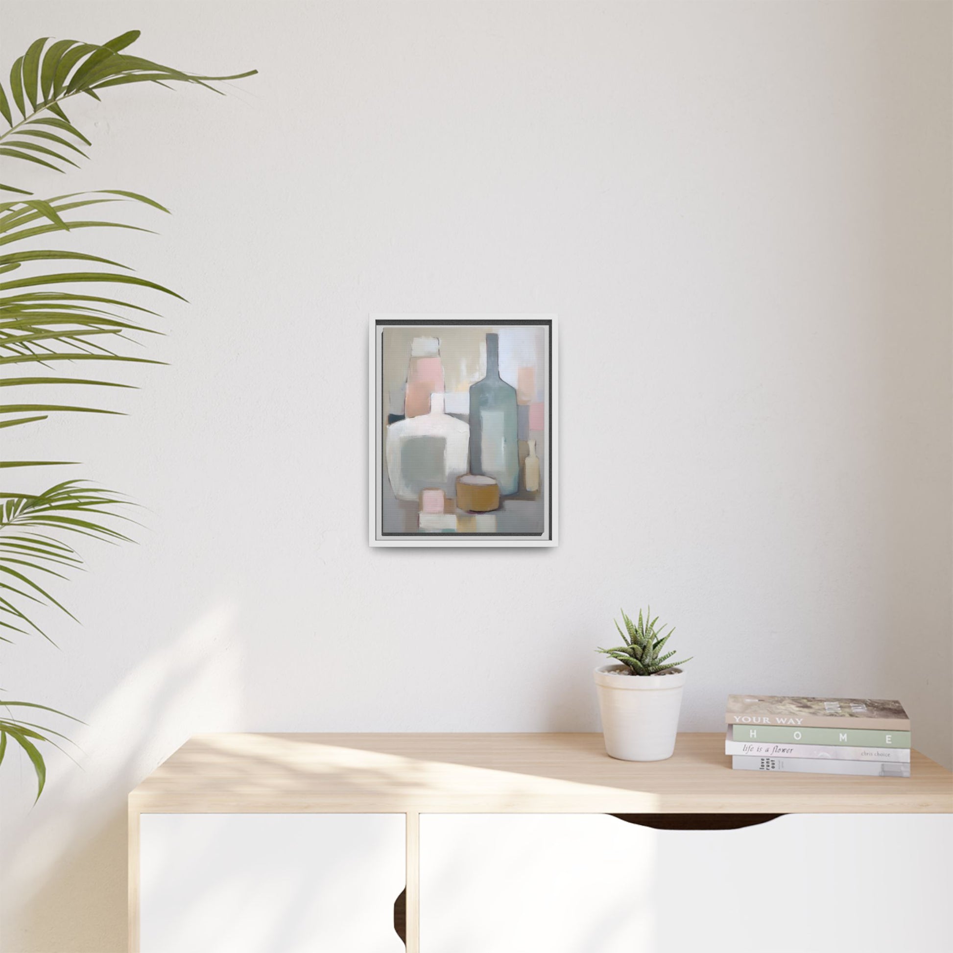 Modern Abstract Bottle Still Life Wall Art – Framed Canvas in Soft Pink, Blue, and Beige hanging on a white wall near plants and books.