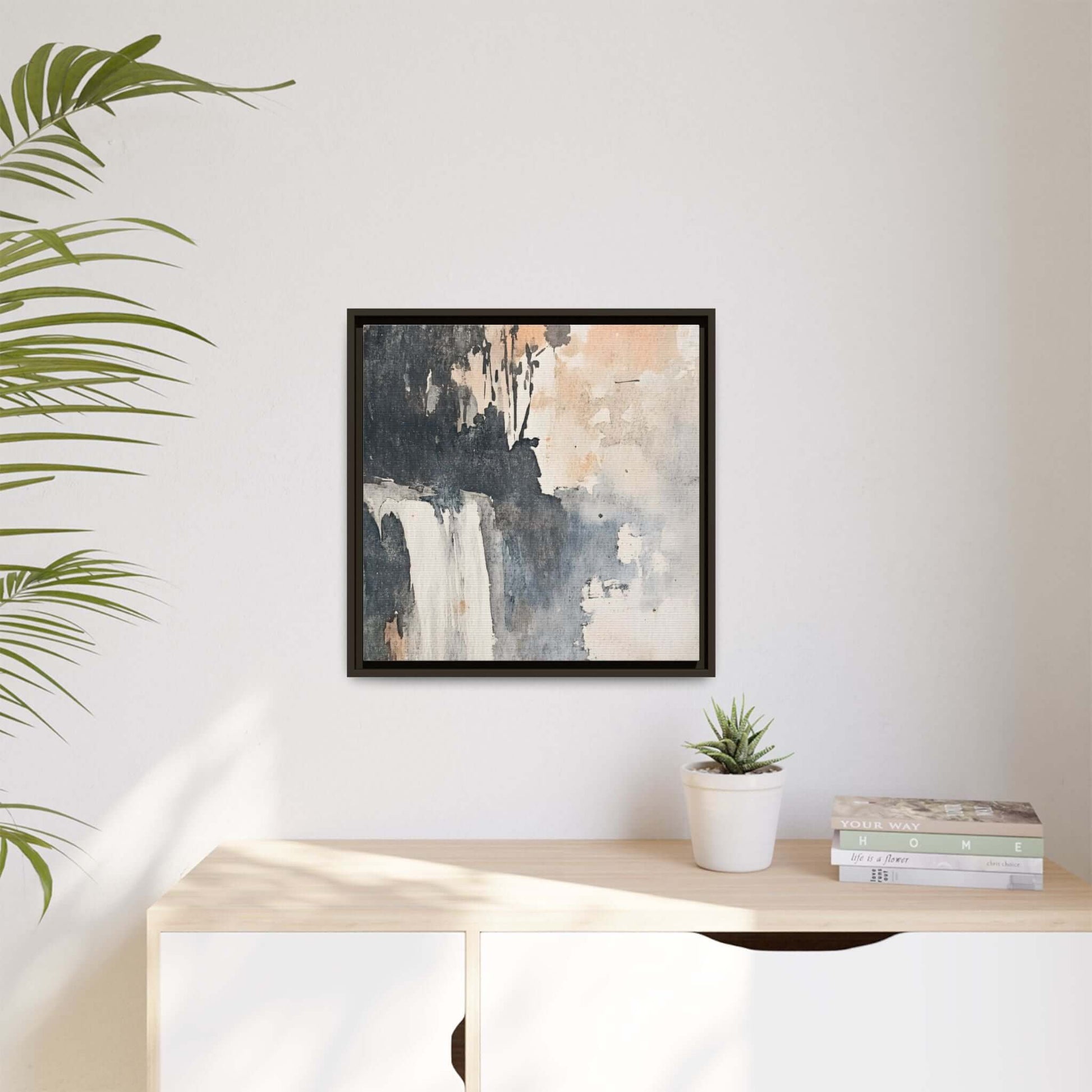 Framed waterfall art print on matte canvas, square decor, displayed on a wall with a plant and books on a wooden shelf.