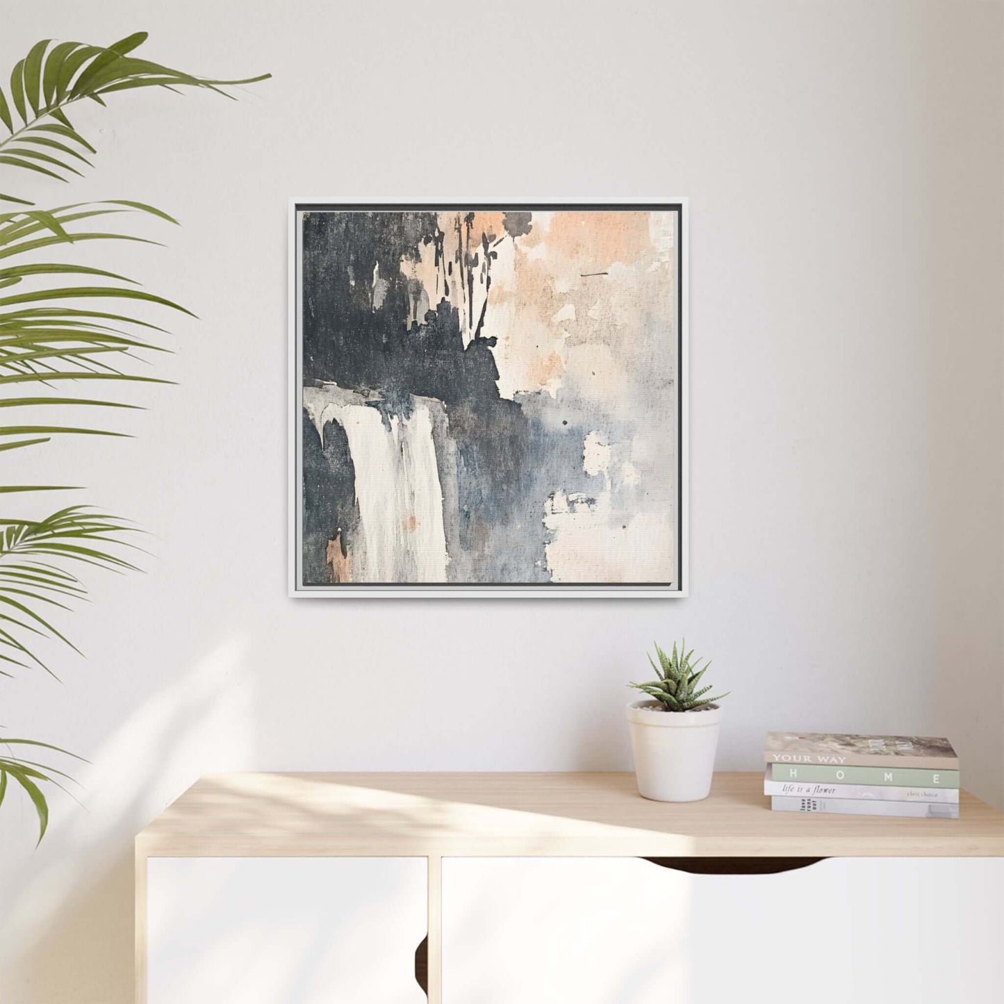Framed waterfall art print in modern home decor setting, matte canvas on wall above a cabinet with plant and books.