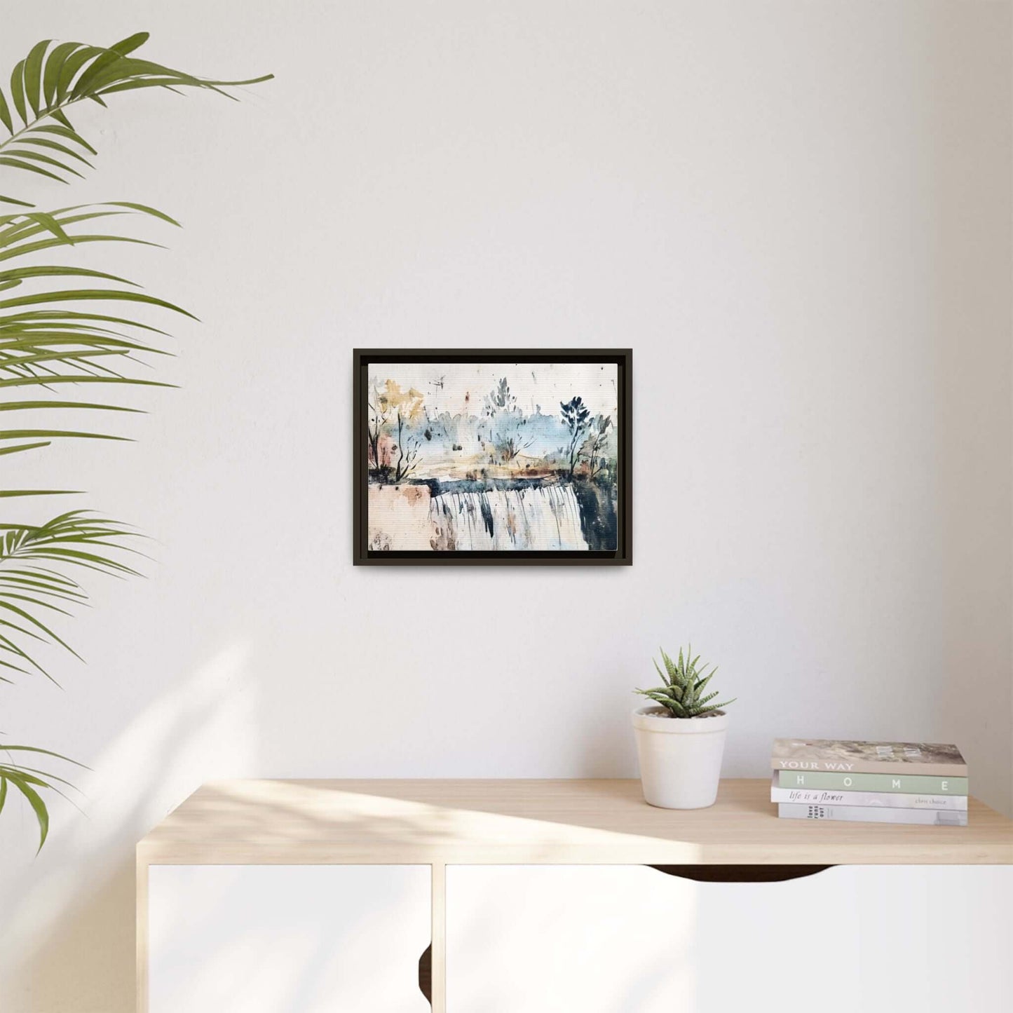 Framed watercolor wall art featuring a serene landscape with trees, displayed in a minimalist room with a plant on a wooden cabinet.