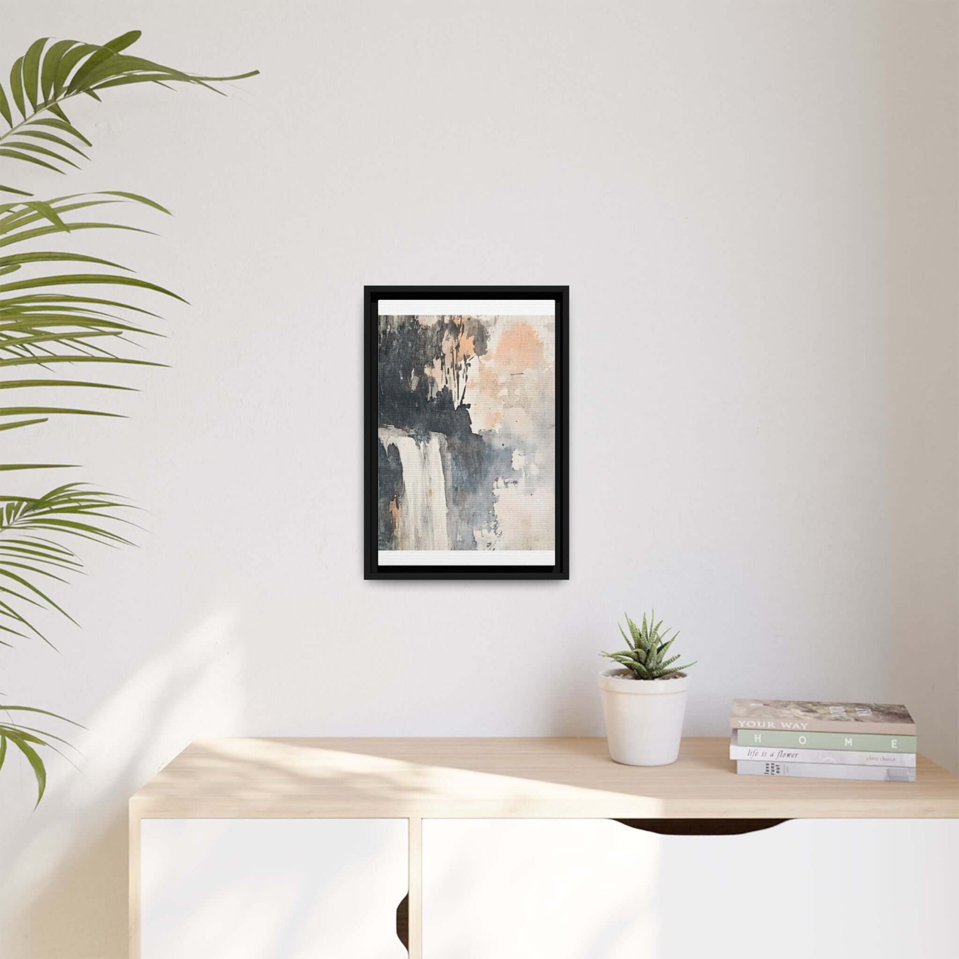 Framed waterfall art print in matte finish displayed on white wall above modern decor table with plant and books.