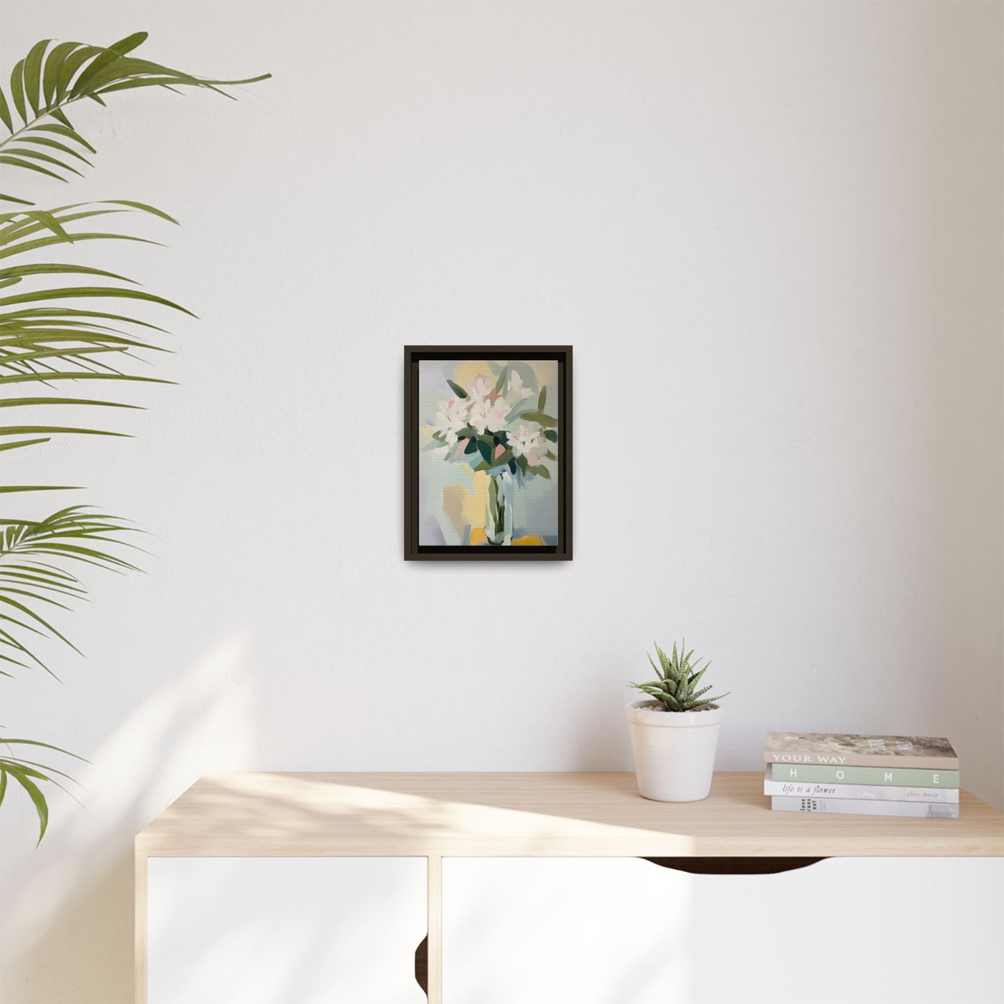 Soft Abstract Floral Wall Art – Framed Modern Canvas with White Flowers in Green Vase on a wall above a light wooden cabinet.