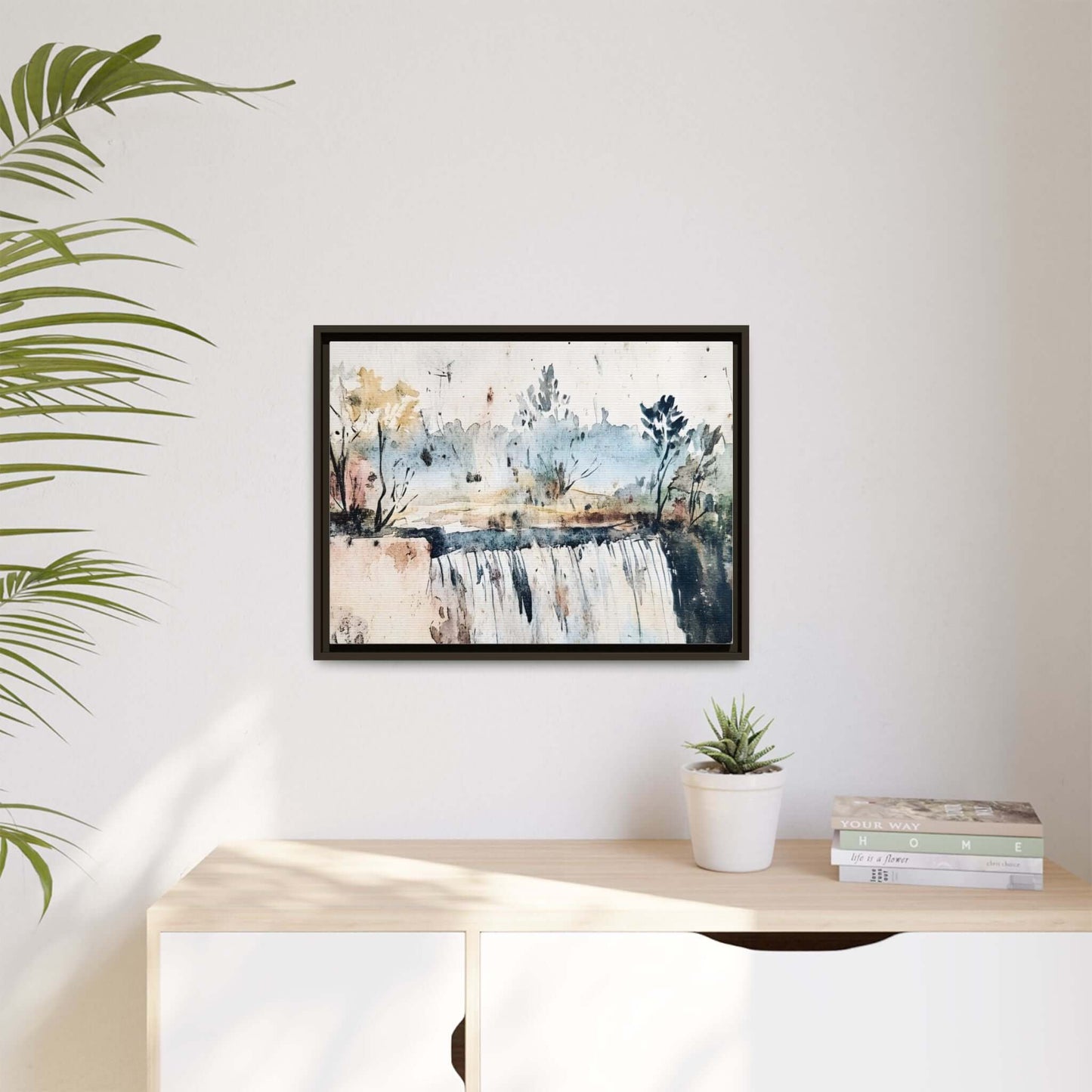 Framed watercolor wall art depicting a serene landscape, featuring soft blue and earthy tones, displayed in a modern room with plants.