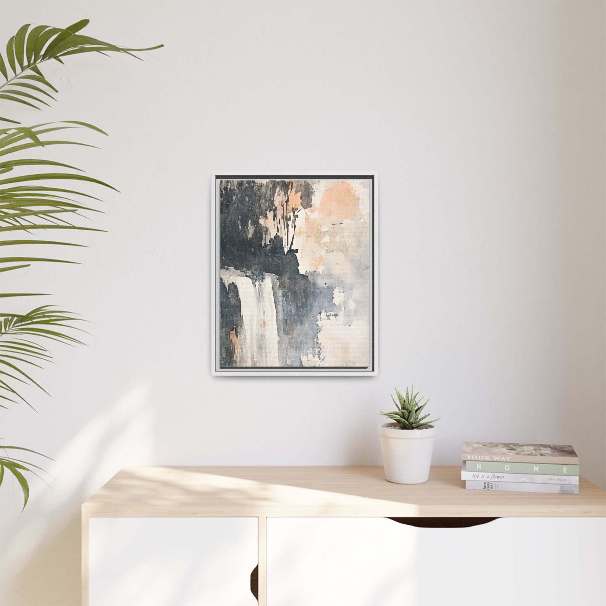 Framed waterfall art print on matte canvas, displayed in a modern home setting with plants and books on a wooden surface.