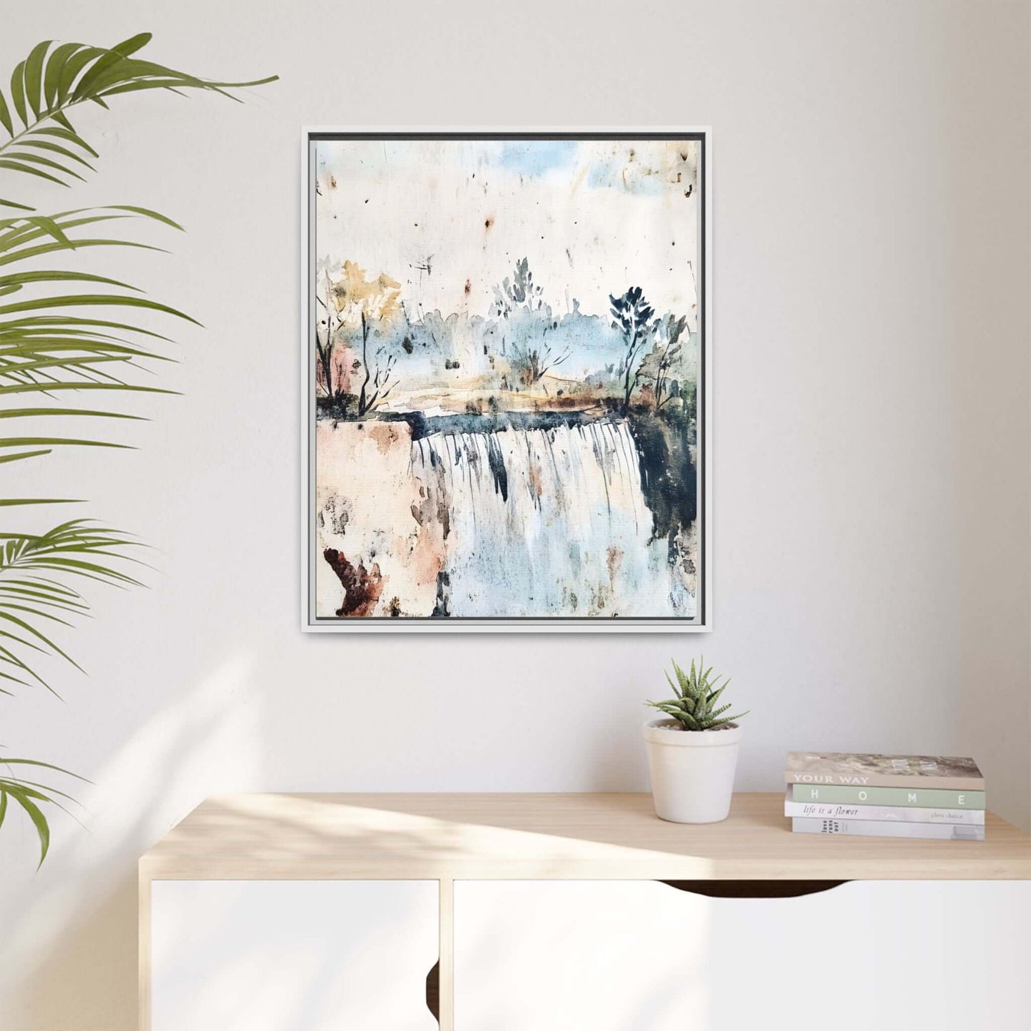 Framed watercolor serene landscape wall art hanging above a modern cabinet with plants and books in a bright, minimalist room.