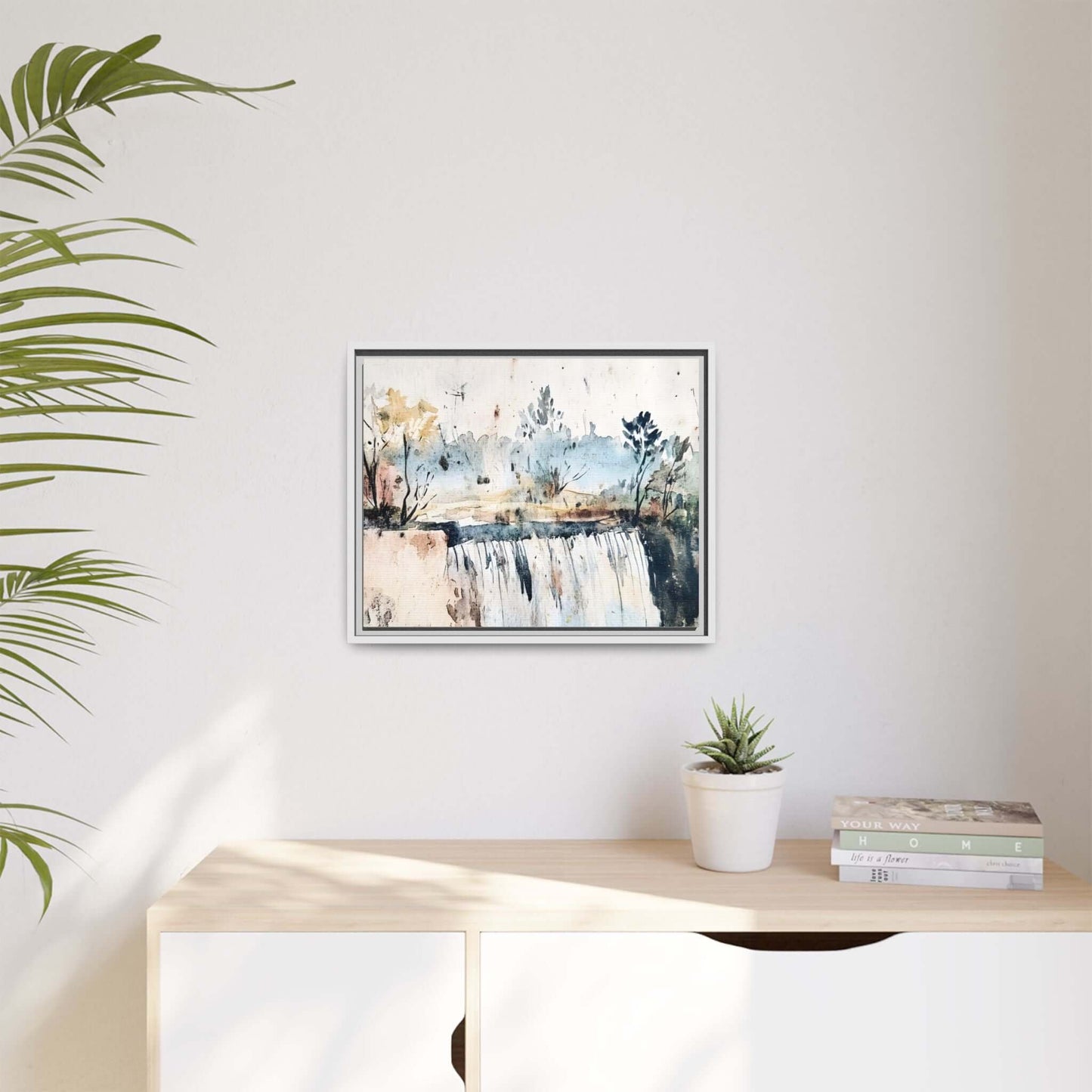 Framed watercolor wall art depicting a serene landscape, hung above a light wooden shelf with a plant and books, creating a tranquil decor setup.
