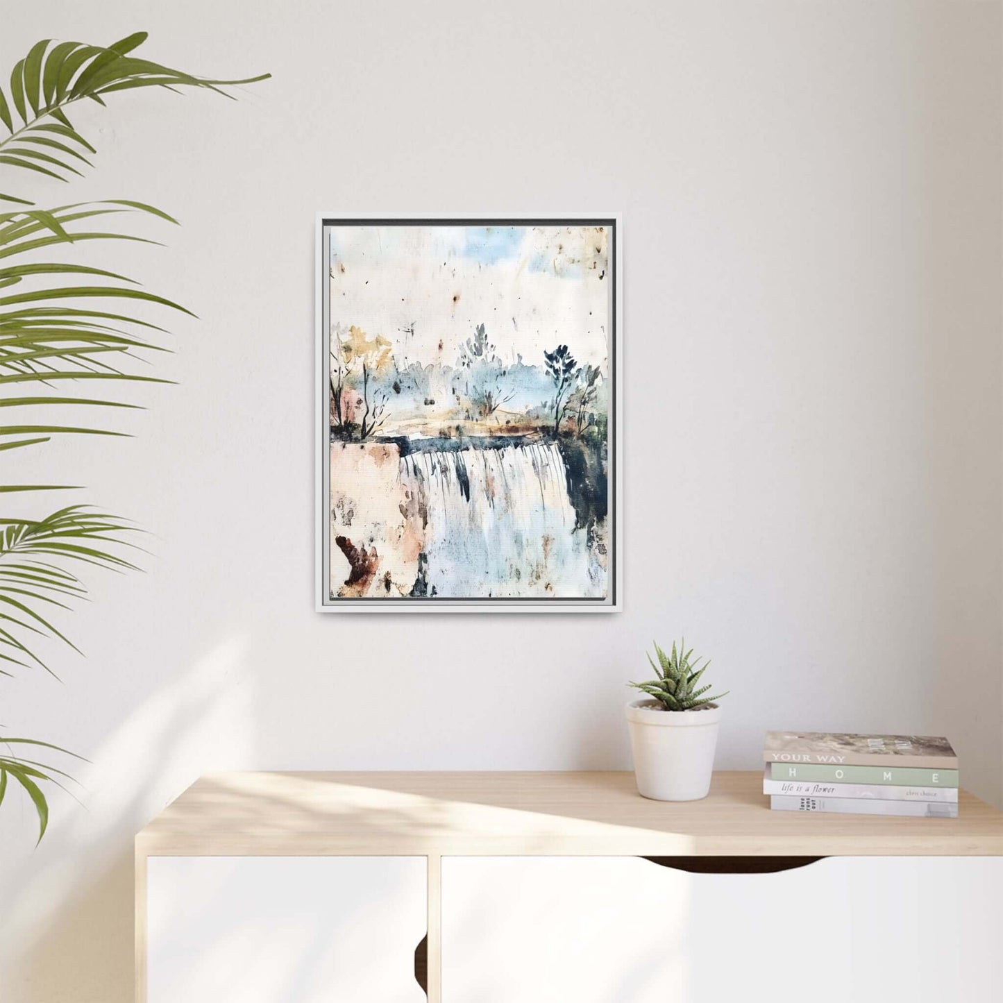 Framed watercolor wall art depicting a serene landscape with trees and water, styled in a modern living room with a potted plant and books.