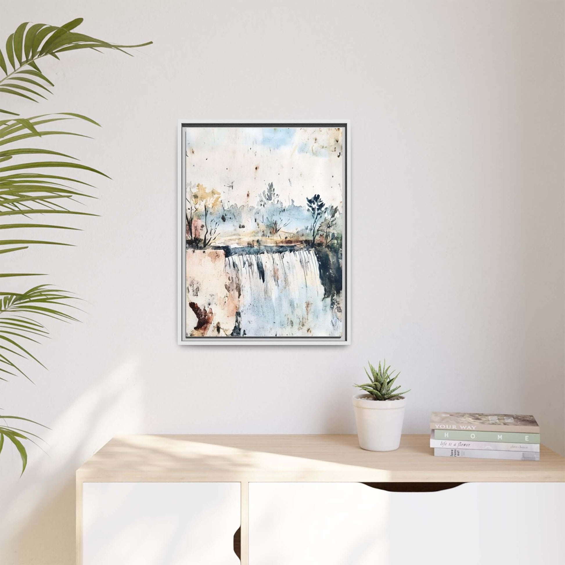 Framed watercolor wall art depicting a serene landscape with trees and water, styled in a modern living room with a potted plant and books.