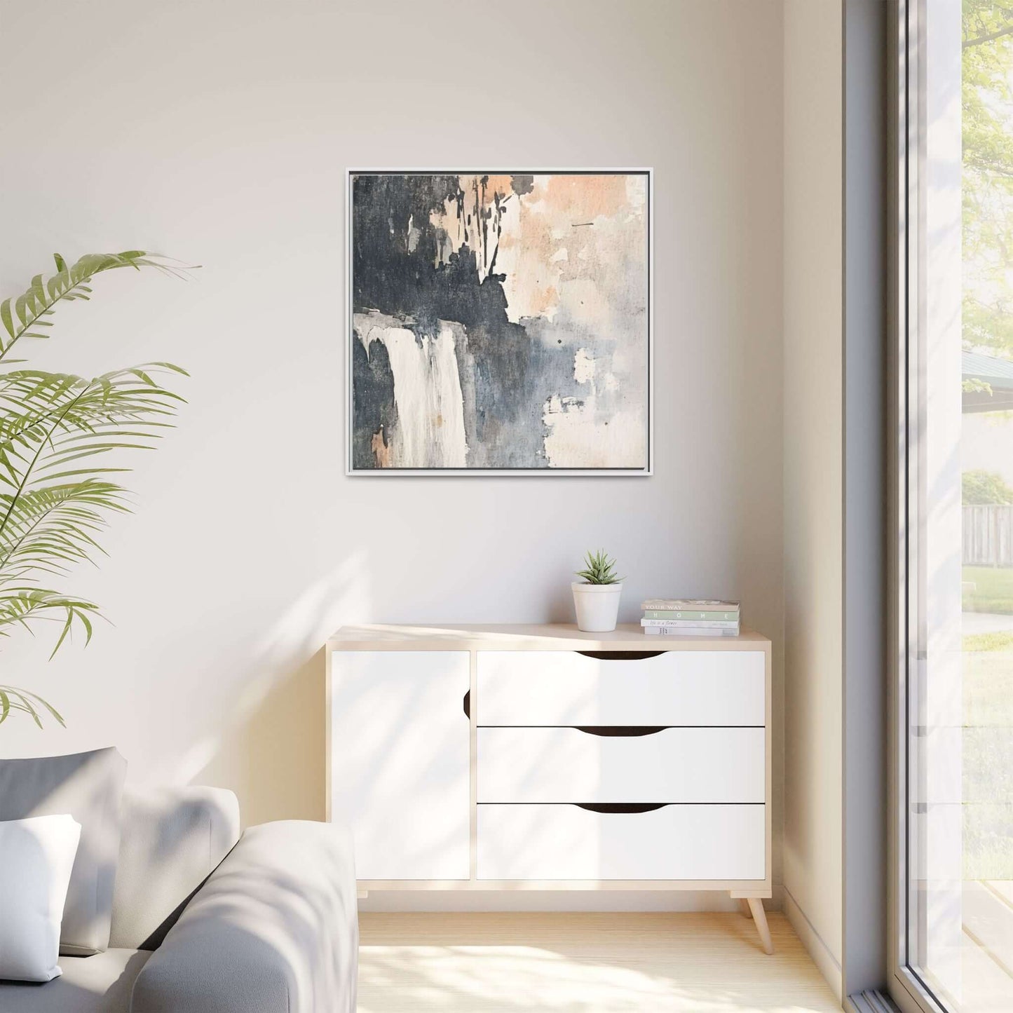 Framed waterfall art print on matte canvas hanging above modern cabinet in bright room with natural light and plant decor.