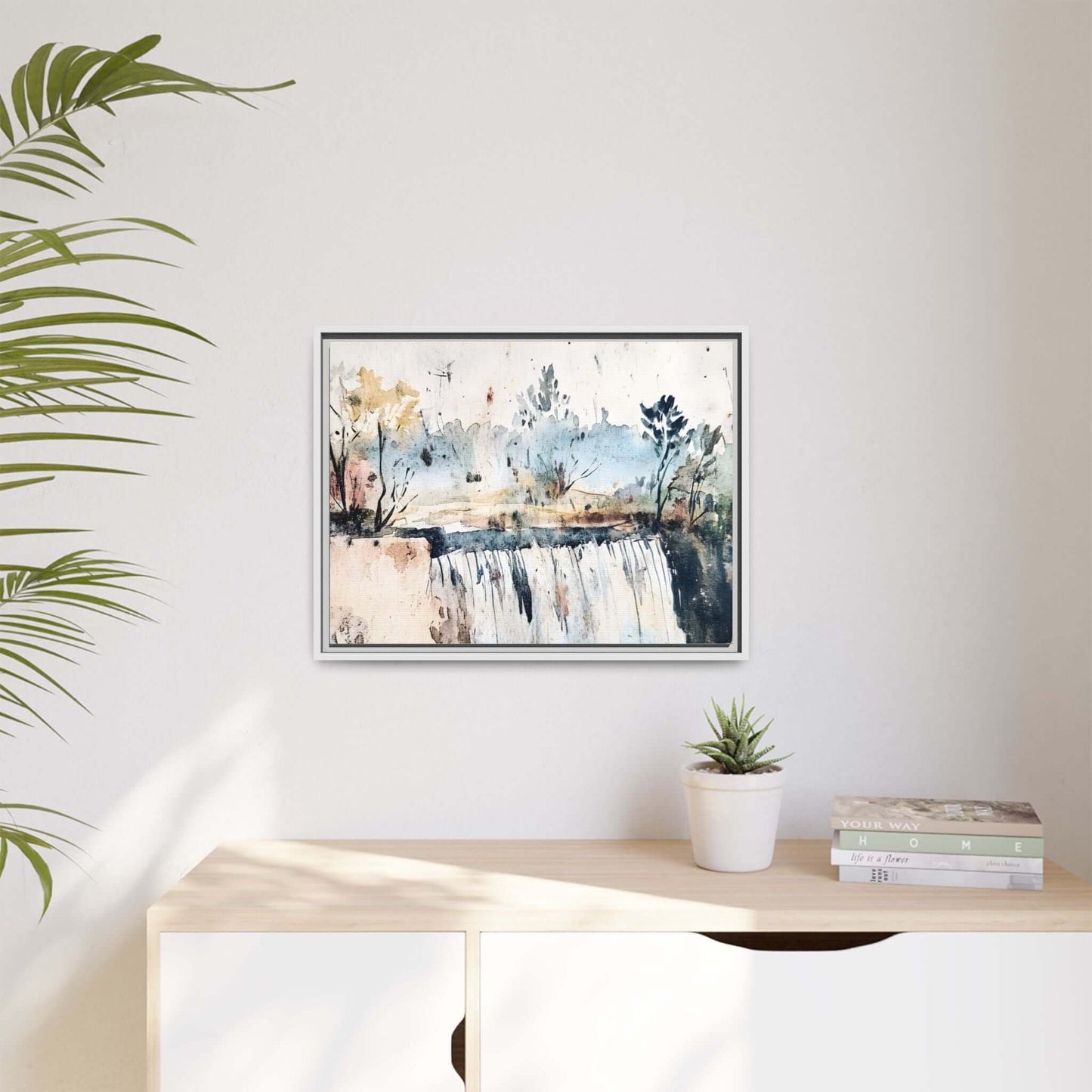 Framed watercolor wall art featuring a serene landscape with trees and a waterfall, displayed on a modern shelf with plants and books.