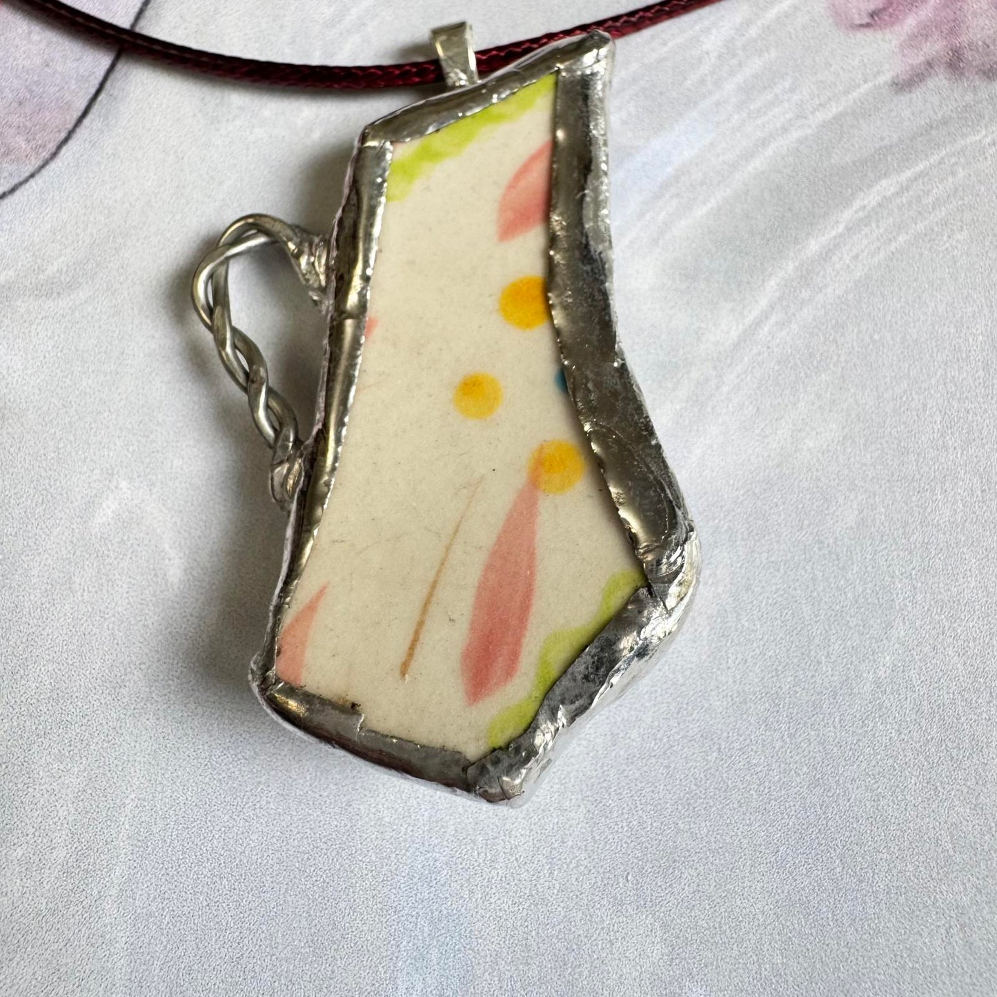 Broken China Teapot Shape Handmade Floral Pendant with pastel floral design on cream background framed in silver-tone metal.