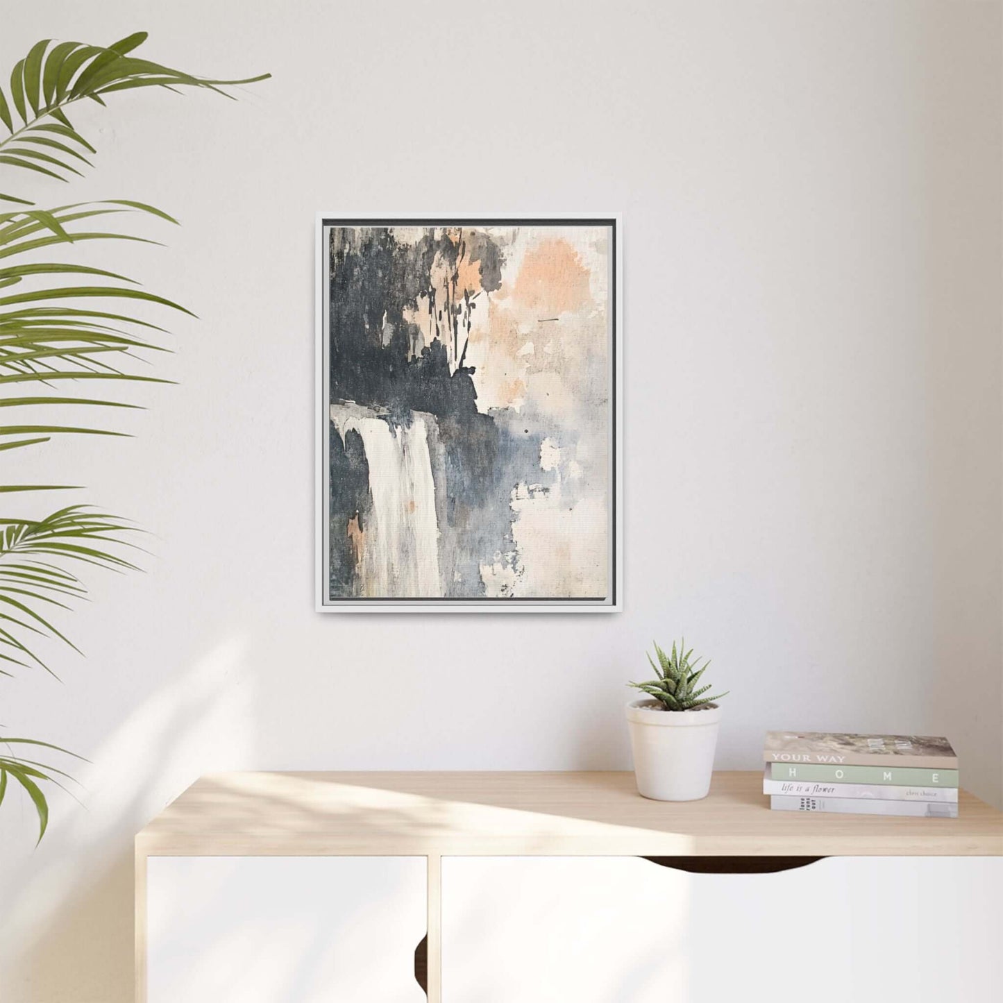 Framed waterfall art print on vertical matte canvas, displayed in a modern home setting with a light wooden console and potted plant.