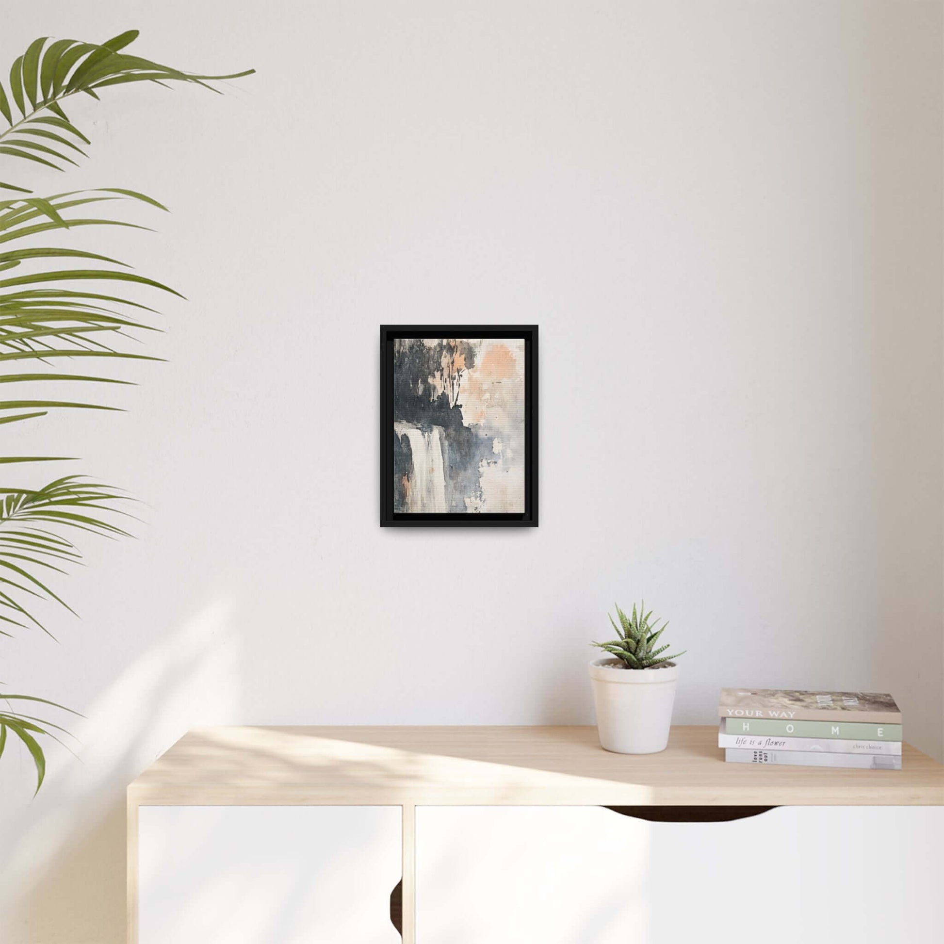 Framed waterfall art print on white wall, surrounded by a plant, books, and a small potted plant, enhancing modern home decor.