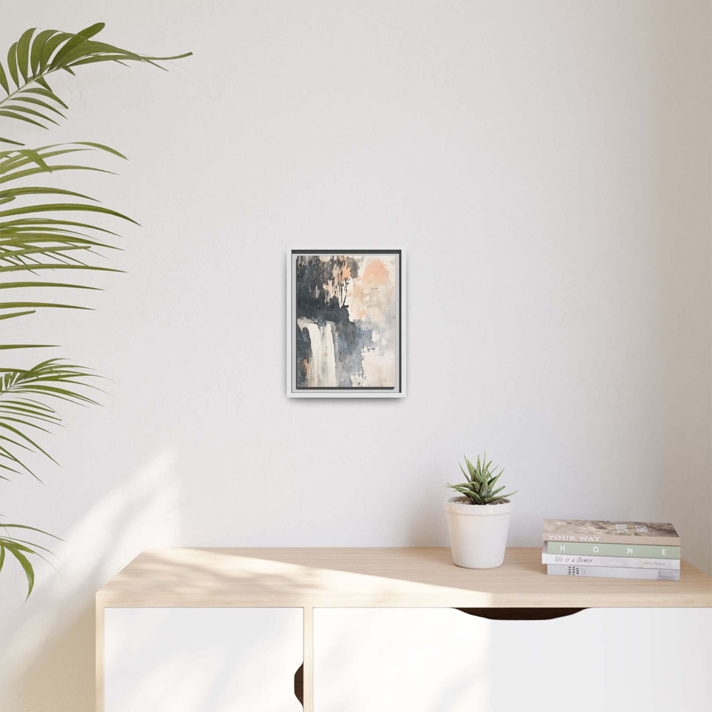 Framed waterfall art print on matte canvas in modern home decor setting, displayed on light wood shelf with plant and books.