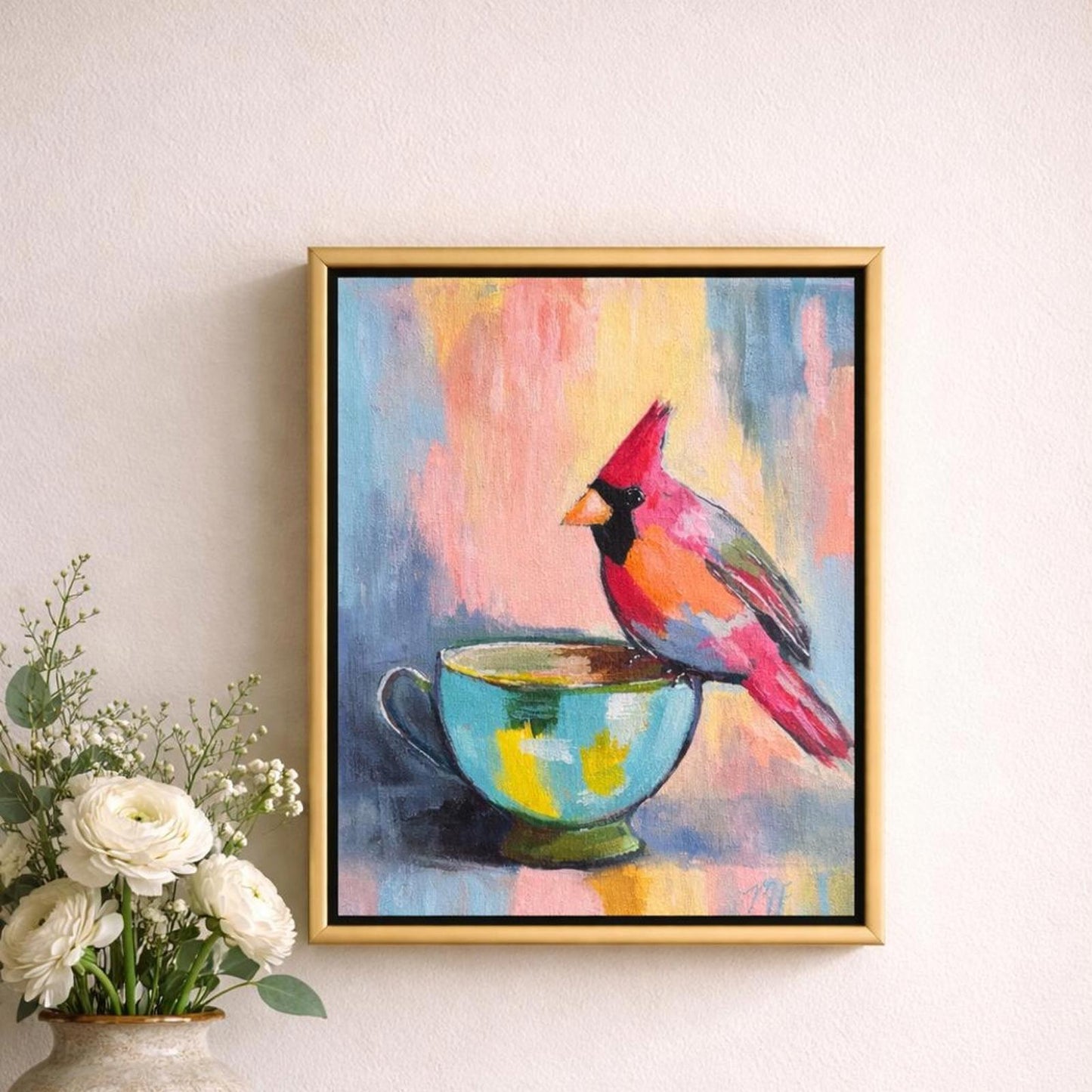 Framed painting of a colorful cardinal bird in a teacup on a wall with flowers below.