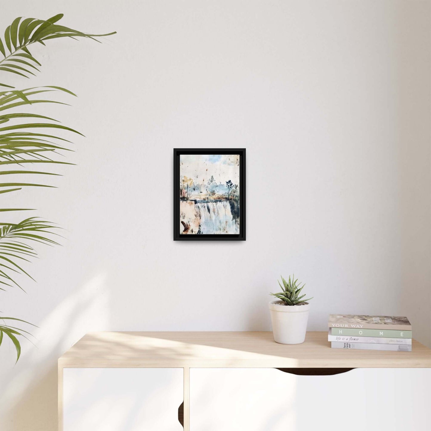 Framed watercolor wall art of serene landscape decor on a minimalist wall, surrounded by a plant and books.