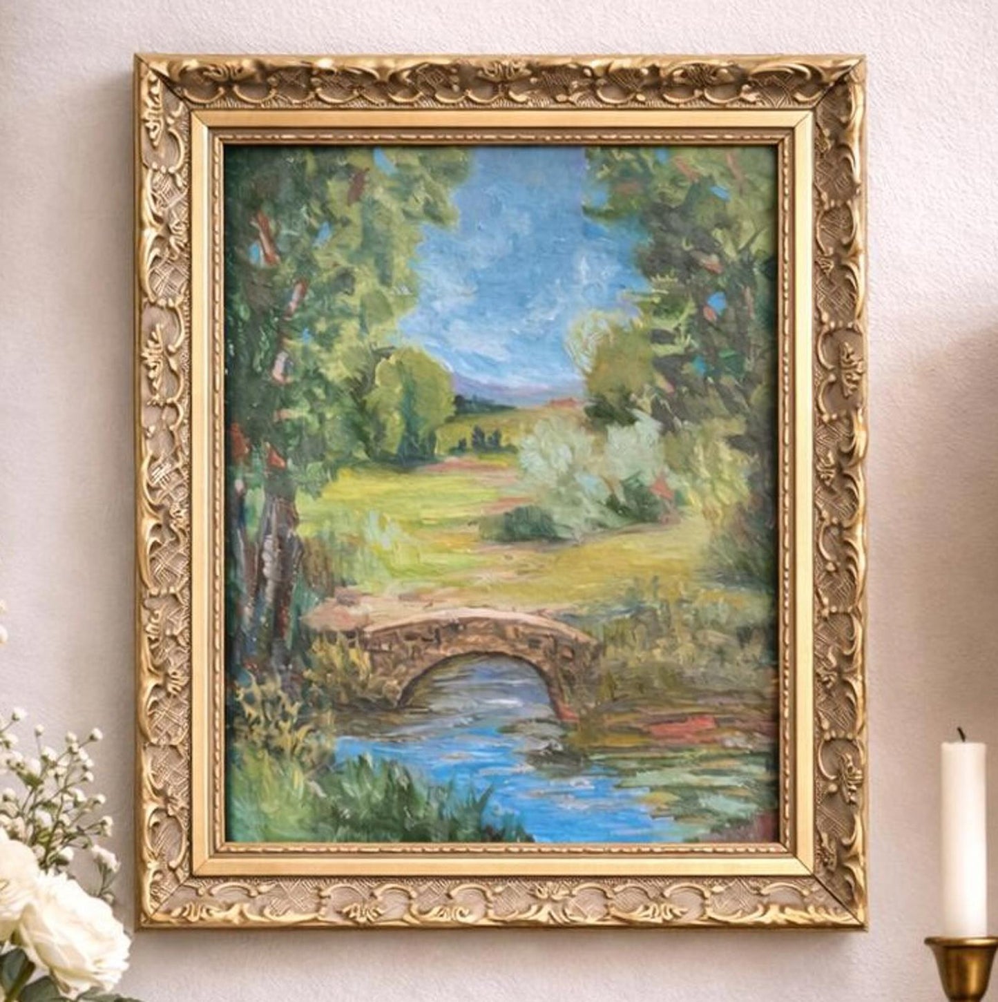 Framed painting of a landscape with a bridge on a wall.