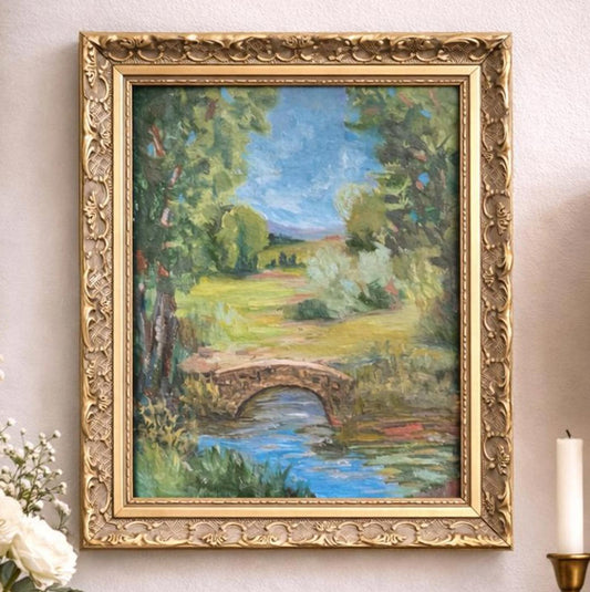 Framed painting of a landscape with a bridge on a wall.