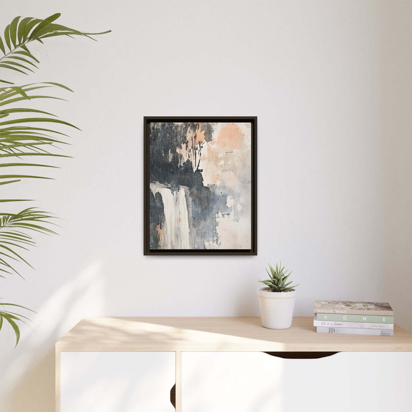 Framed waterfall art print on matte canvas, displayed in minimalist home decor setting with plants and books.