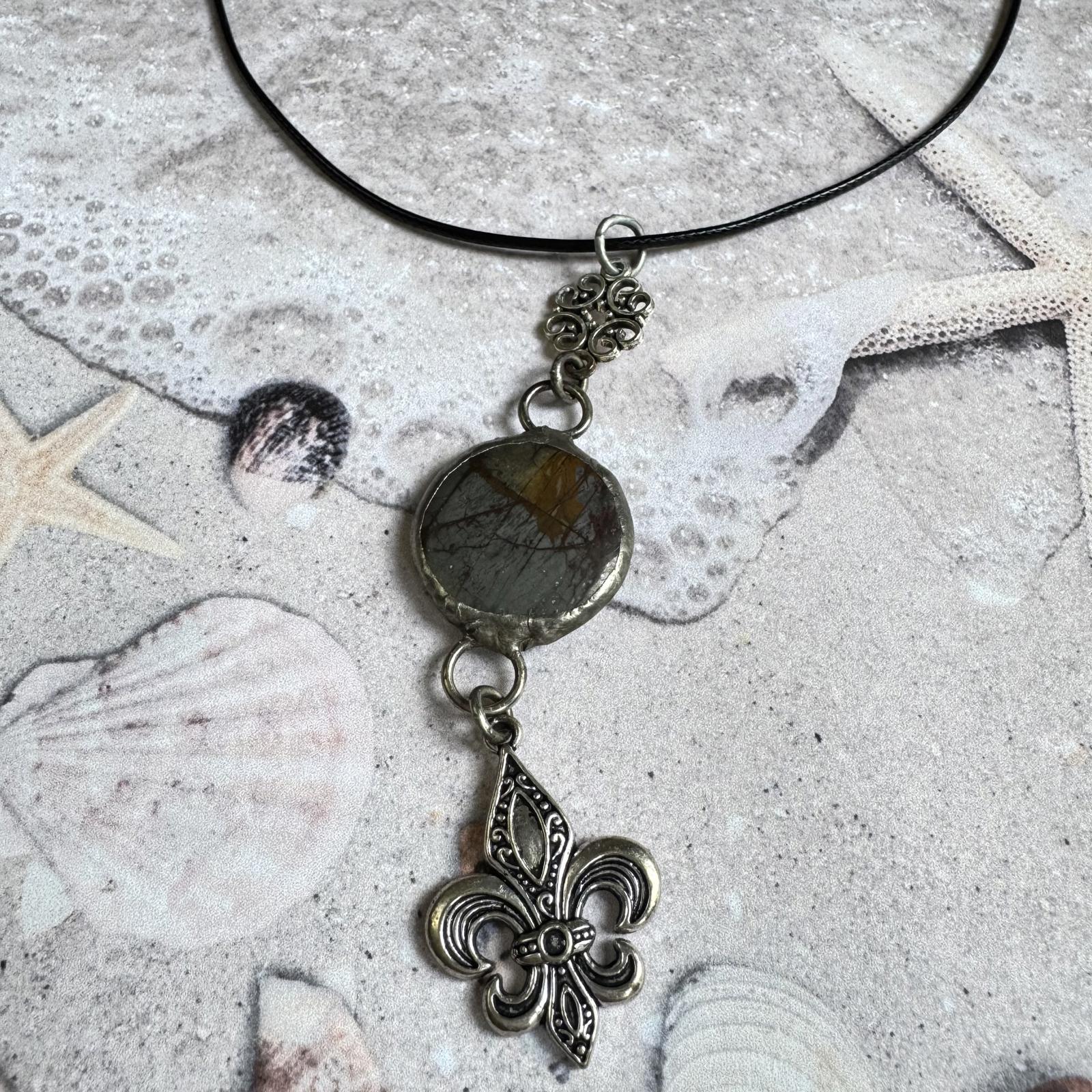 Handmade Natural Stone with Silver Tone Fleur-de-Lis Pendant on beach-themed background.