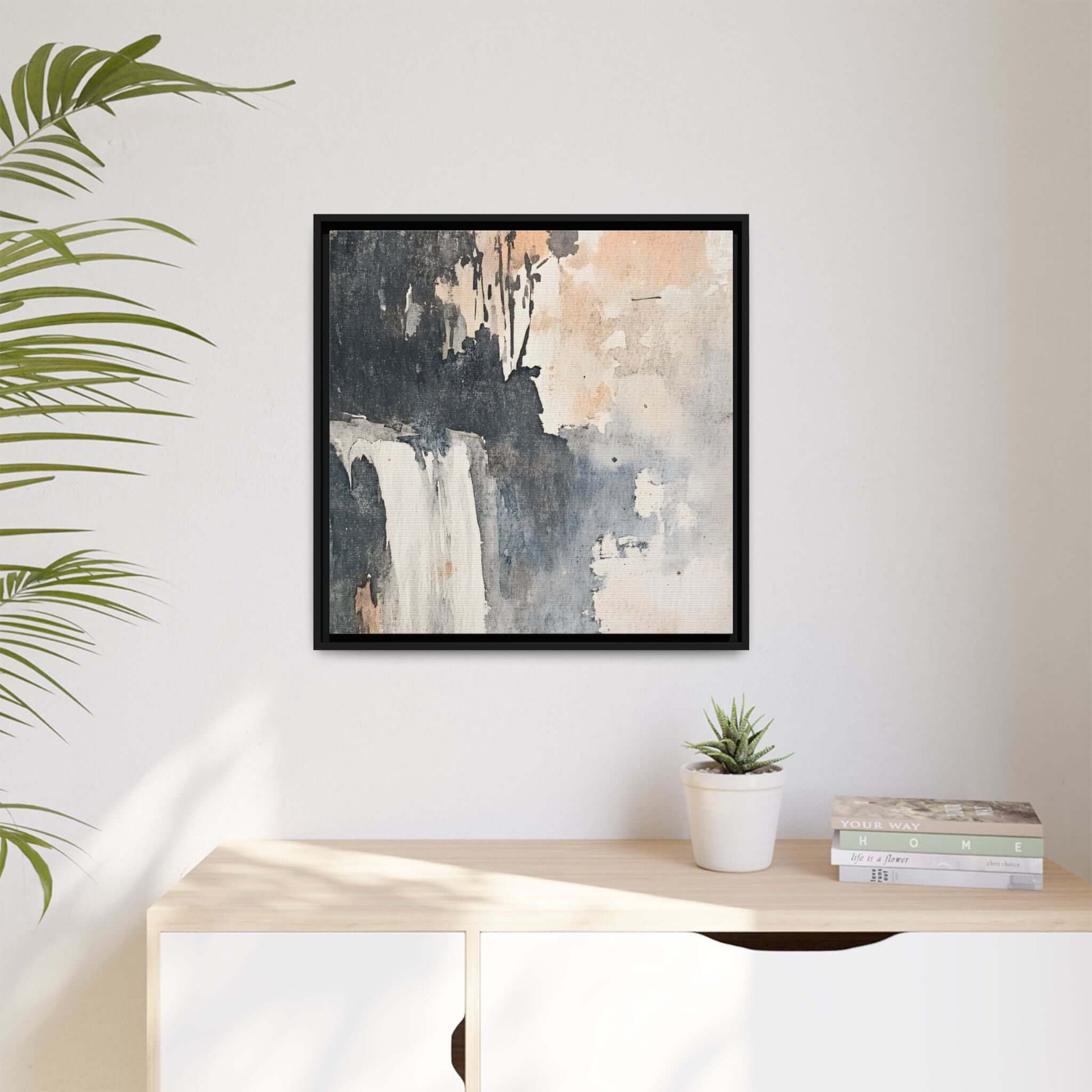 Framed waterfall art print on a matte canvas displayed on a wall, with a plant and books on a nearby table.