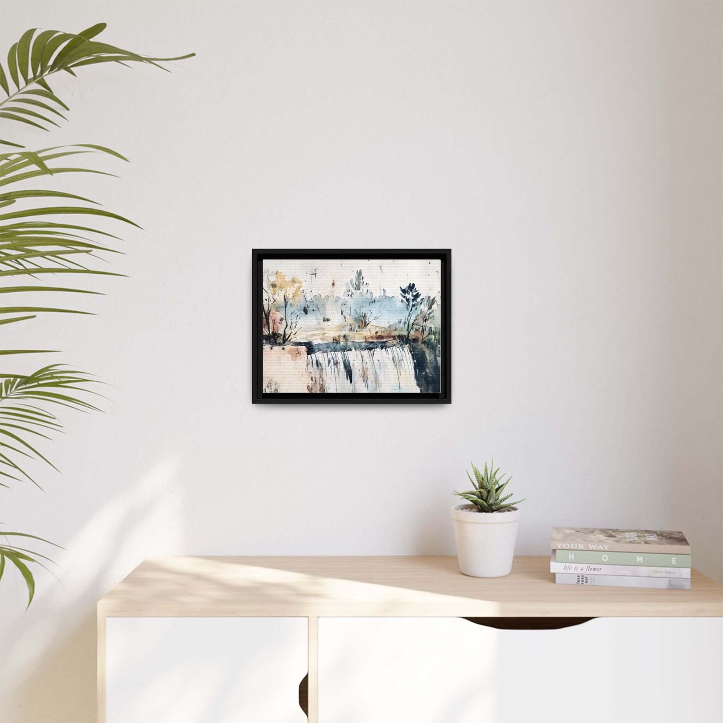Framed watercolor wall art with serene landscape decor hanging on a modern white wall, beside a plant and books on a light wood shelf.