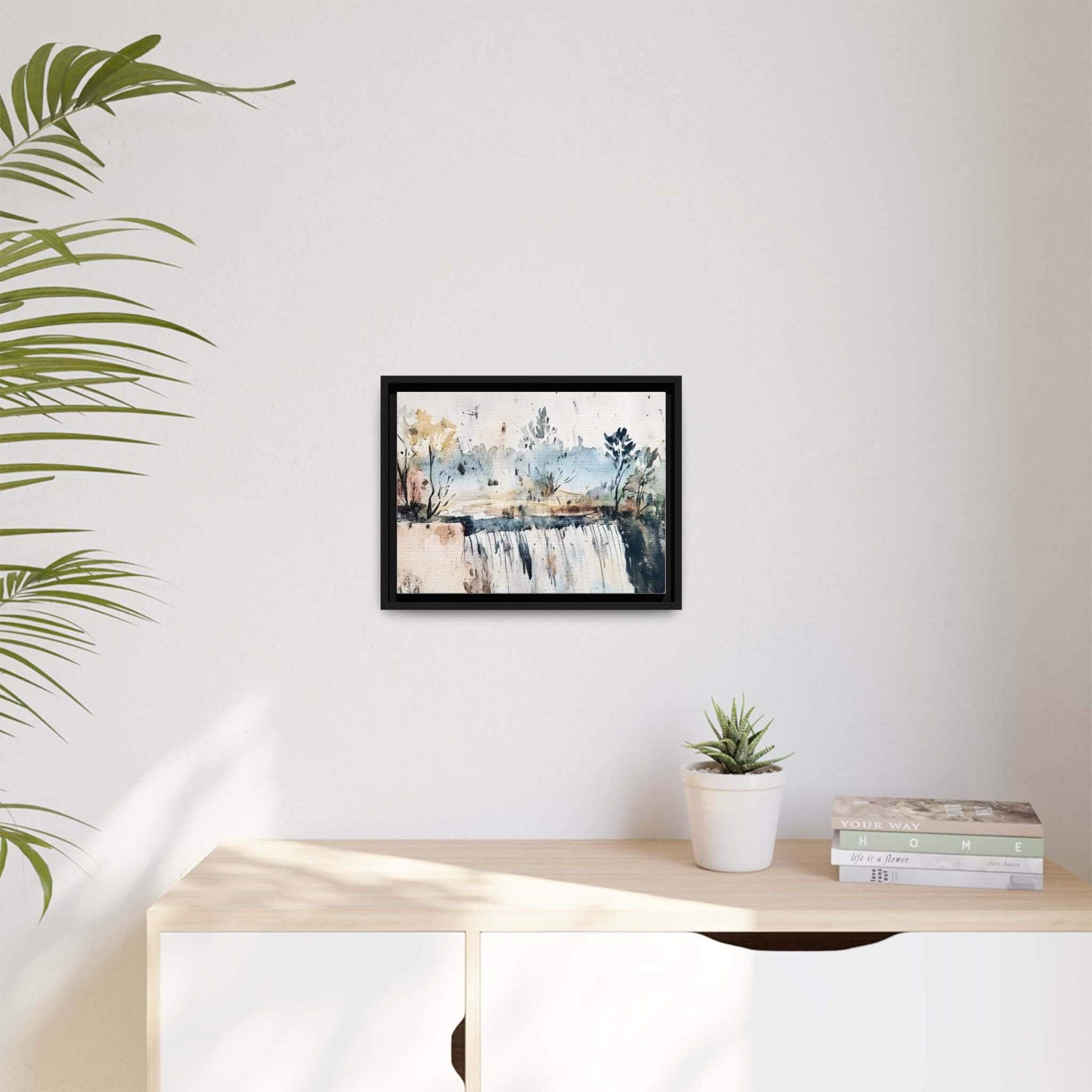 Framed watercolor wall art with serene landscape decor hanging on a modern white wall, beside a plant and books on a light wood shelf.