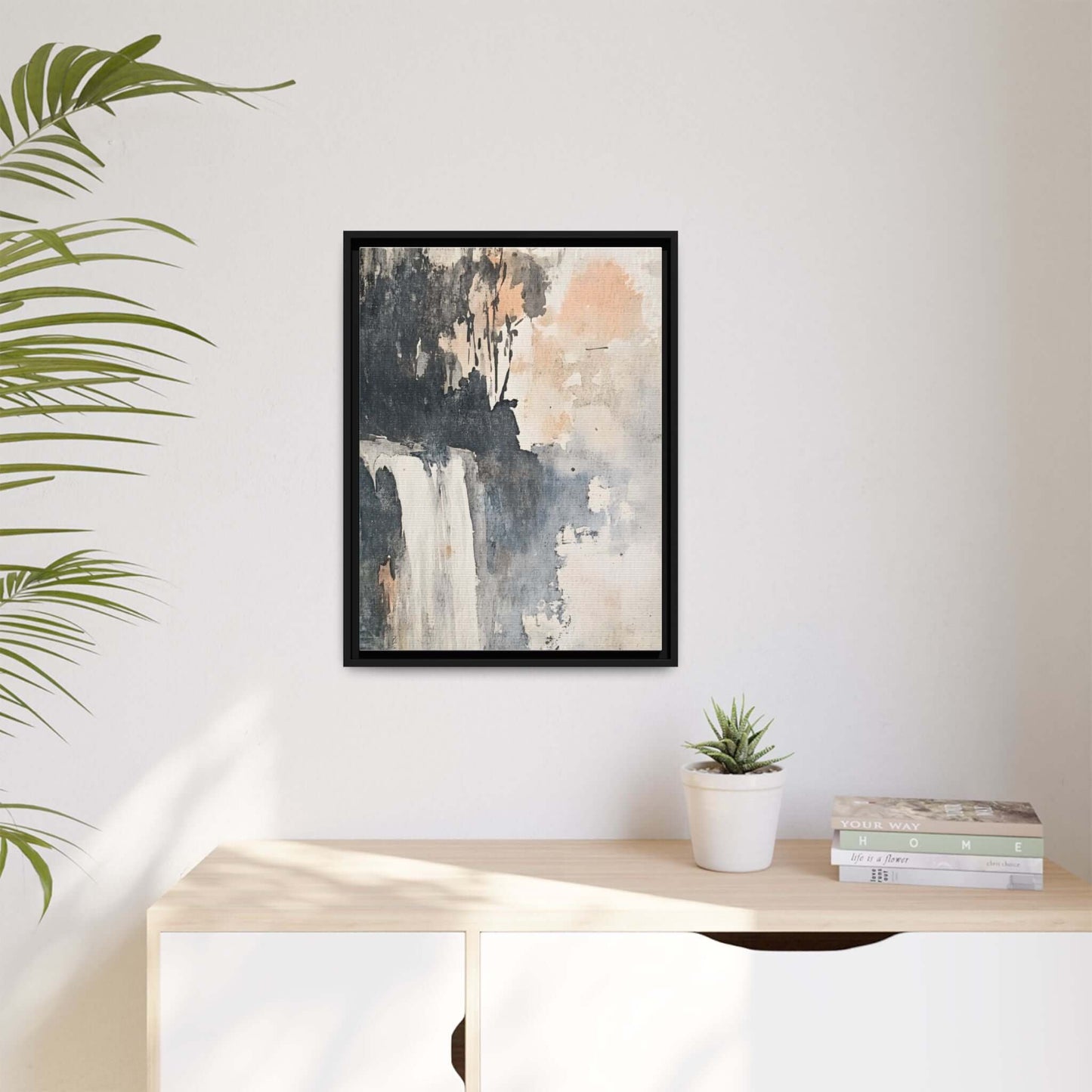 Framed waterfall art print on matte canvas hanging in a modern home interior with plants and books on a wooden table.