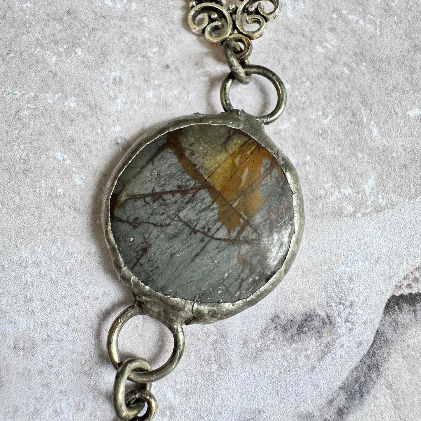 Handmade Natural Stone with Silver Tone Fleur-de-Lis Pendant featuring gray and amber hues on black cord.