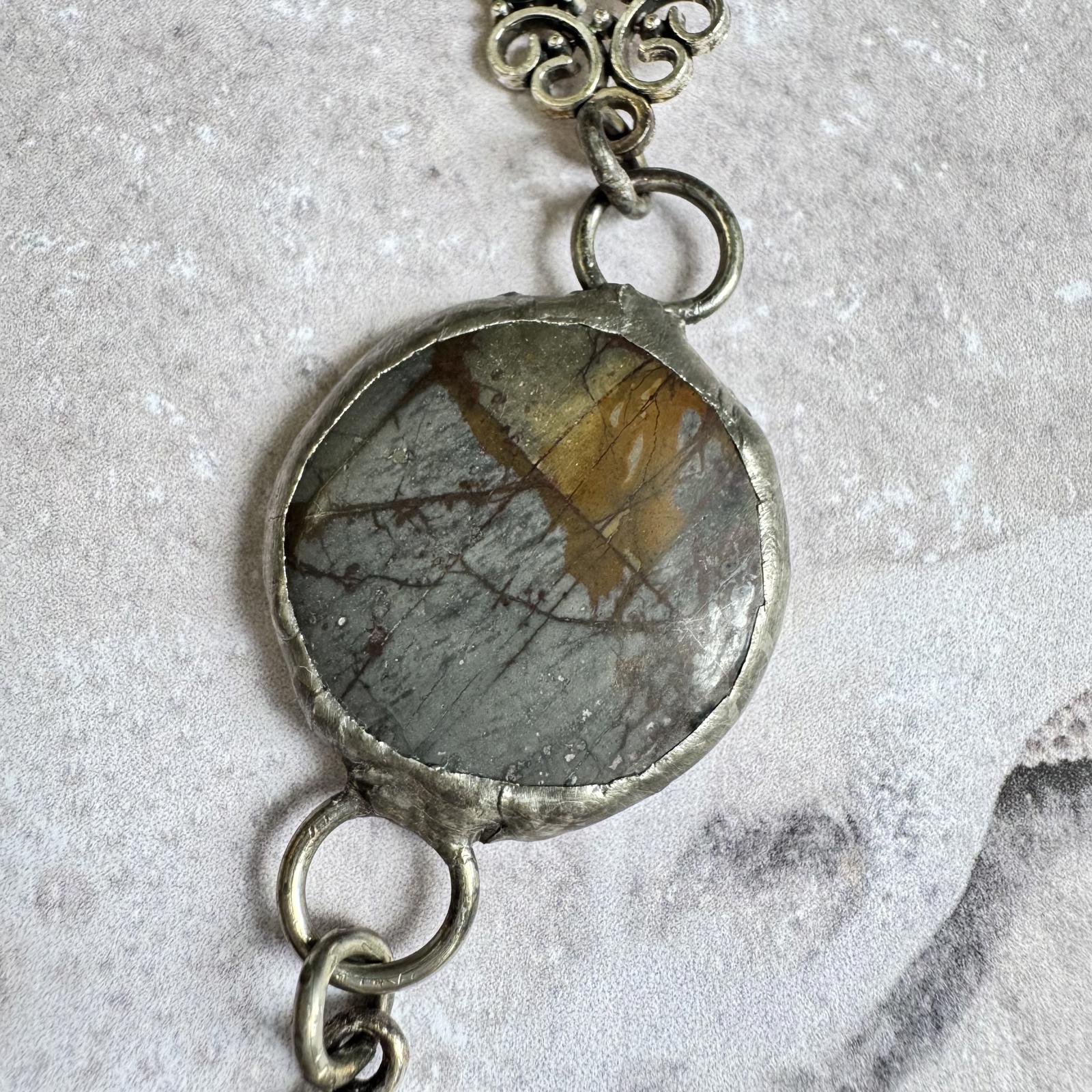Handmade Natural Stone with Silver Tone Fleur-de-Lis Pendant featuring gray and amber hues on black cord.